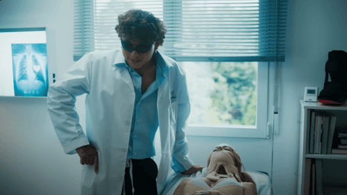 Beéle, con bata de médico, y Tini, acostada en la cama con una férula.