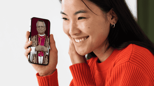 Mujer con celular en la mano. En la pantalla se ve el atuendo del nuevo papa, León XIV.